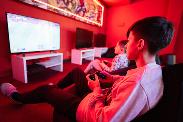 Two boys gamers play football gamepad video game console in red gaming room.