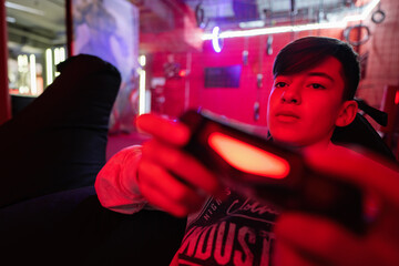 Teenager boy gamer play gamepad video game console in red gaming room.