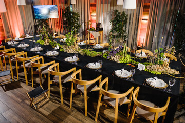 Fototapeta na wymiar Table decorated plates and glasses, candle, flowers, greenery. Interior of table for guests with natural decor. Reception. Rustic. Composition of bark tree, wooden decor, moss in restaurant. Top view.