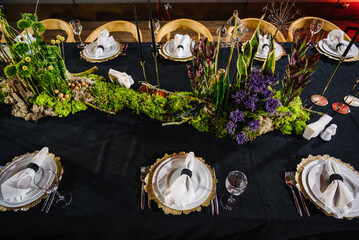 Table decorated plates and glasses, candle, flowers, greenery. Interior of table for guests with natural decor. Reception. Rustic. Composition of bark tree, wooden decor, moss in restaurant. Top view.
