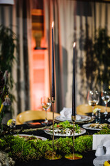 Candles. Table decorated plates and glasses, candle, flowers, greenery. Interior of table for guests with natural decor. Reception. Rustic. Composition of bark tree, wooden decor, moss in restaurant.