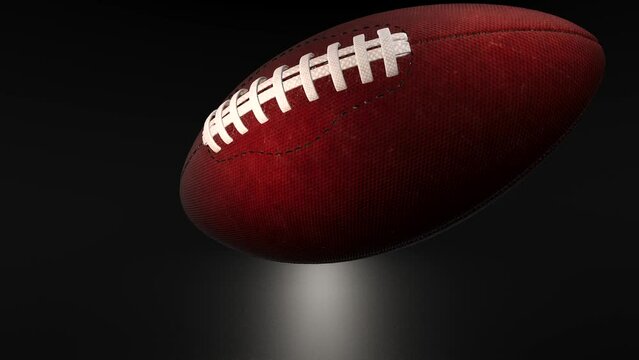 American football in slow motion moving away from the camera over a black background.