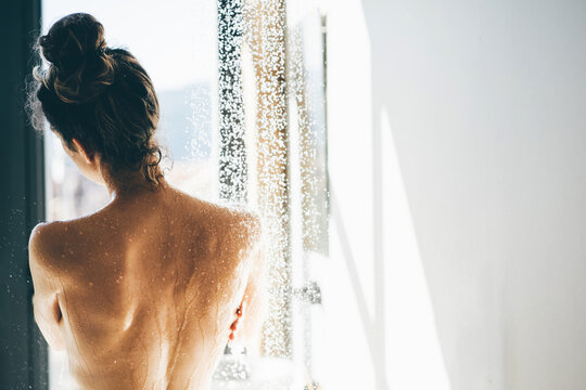 View from behind of young sexy naked woman in shower. Water drops falling on her back close up.