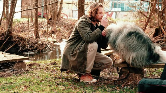 Much in love, the blond young man looks at his best friend. The gray, fluffy wolf spitz eats a treat from his friend's hand. An autumnal brown forest and a beautiful weather give this shot much charm