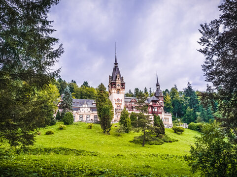 Front View Of The Peles Castle With Trees And Bushes In The Foreground