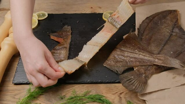Women's hands remove the scales from a piece of dried fish of the flounder family and show it to the camera. Fish Murmansk ruff.