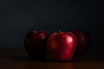 Three red apples on the wood table and dark grey background.