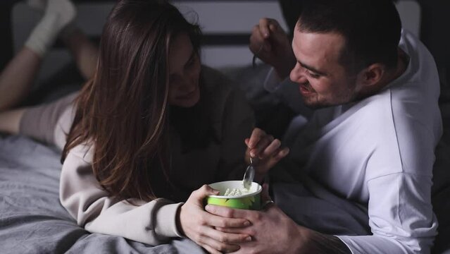 Cheerful couple eating pistachio ice cream lying in the bed at home and talking. Dating. Couple have fun at home. Love relationship concept.