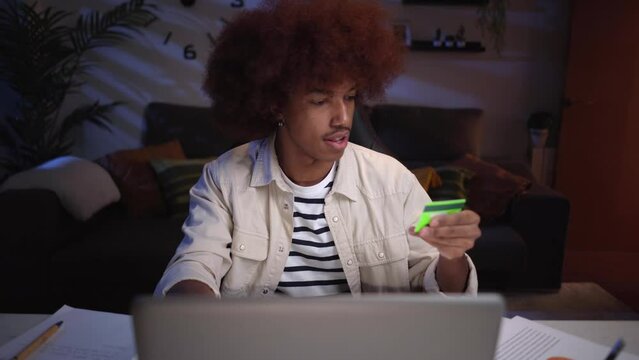 Young Afro American man at home office, using credit card to do online payment and buy on-line courses. Concept of E-learning.