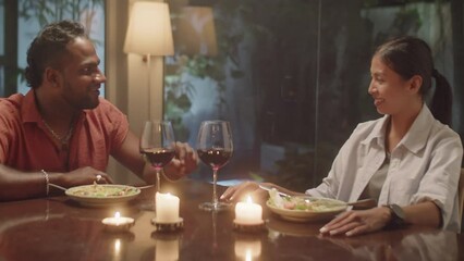 Medium shot of diverse family couple sitting at dinner table with food, wine and candles and having discussion over meal in evening at home - Powered by Adobe