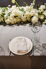 Wedding setup detail. Festive table covered tablecloth, decorated composition flowers and candles in party area. Table setting, serving. Banquet decoration in hall restaurant. Luxury reception.