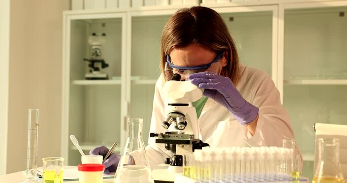 Scientist biologist works on microscope and writes notes in laboratory. Molecular biology research and virology