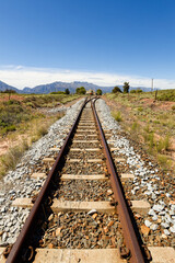 Fototapeta premium A view along railroad tracks towards high mountains in the distance, near Worcester, South Africa.