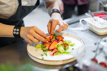 Chef cooking Green salad with salmon, cucumbers, lettuce, spices, caviar on restaurant kitchen