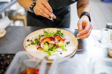 Chef cooking Green salad with salmon, cucumbers, lettuce, spices, caviar on restaurant kitchen