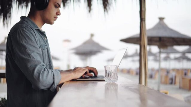 Closeup of devloper man hands typing, coding on a laptop while on in a beach bar, business freelancer working on vacation