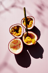 Fresh passion fruit with golden spoon. Sun light, dark long shadow, top view. Light pink...