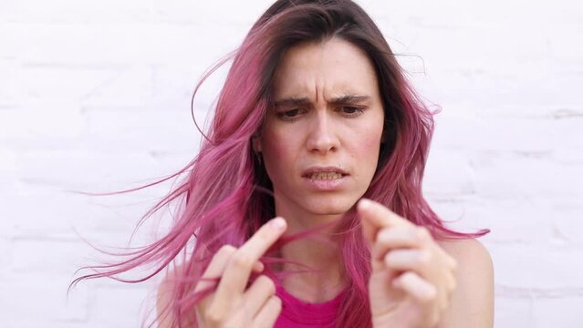 Depressed young woman looking at split pink hair ends. Worried sad girl feels upset about brittle damaged dry hair loss concept. Female hormone problems concept.