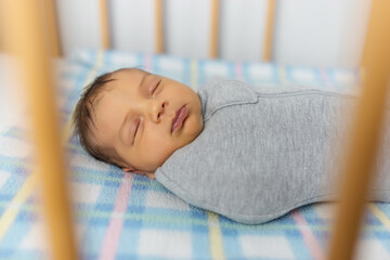 The baby is lying in a cocoon on cot. He sleeps sweetly and dreams.