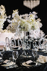 Table number 6. Setting, and serving guests closeup. Stands, sign number six. Closeup. Wedding setup detail. Festive table covered black tablecloth, decorated composition flowers in party area.