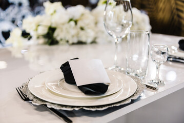 Serving, setting table. Plate decorated linen black napkin, postcard, silverware cutlery, glasses. Side view. Closeup. Wedding set up, dinner table reception. Birthday, baptism, event.