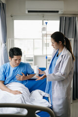 Fototapeta premium Doctor and young male patient who lie on the bed while checking pulse, consult and explain with nurse taking note in hospital