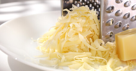 grated cheese with a grater on a white plate. a piece of hard cheese next to shredded cheese close-up. parmesan cooking process.
