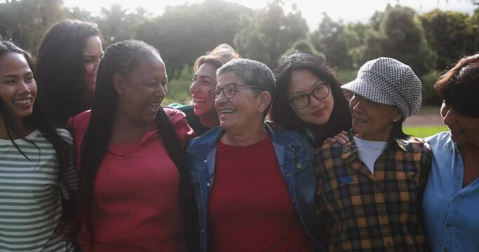Group of multigenerational women hugging each other outdoor - Multiracial female friends with different ages having fun together at city park 