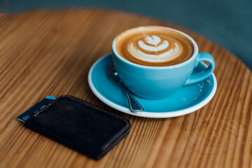 Blue mug cappuccino and coffee art with wallet and credit card lying on a wooden table. Top view. 
