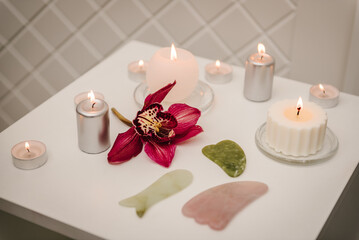 Gua sha tool. Candles, and orchid flowers on table. Facial massage for lifting, face therapy, home spa, mockup. Skincare concept. Cosmetology, body massage, spa procedure. Details decor in spa salon.
