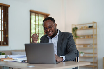 middle aged man American African business man holding computer laptop with hands up in winner is gesture, Happy to be successful celebrating achievement success