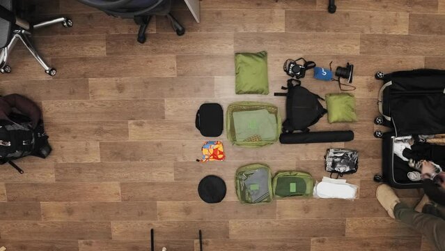 Man is packing backpack and suitcase gathering clothes from the floor preparing for trip filmed in timelapse. Top view of caucasian person anticipating future holiday. Travelling with necessary things