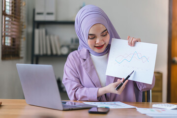 Portrait of a beautiful Muslim millennial Asian businesswoman wearing a purple hijab working remotely from her home office.