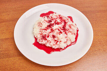 Rice porridge covered with raspberry jam on a white plate.