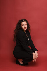 fashion female portrait. Girl, curly girl with black hair in a strict business suit on a red, pink background. High quality photo