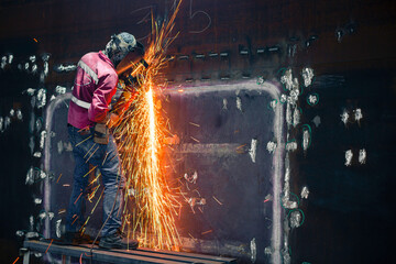 Worker using electric wheel spark grinding on welder metal carbon steel part shell plate inside tank