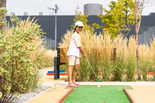 Cute preschool girl playing mini golf with family. Happy child having fun with outdoor activity. Summer sport for children and adults, outdoors. Family vacations or resort.