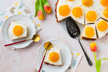 Homemade German Fried Egg Cake Spiegeleierkuchen with apricot and milk pudding on a light background with tulips. Traditional Easter Dessert. Festive Easter food.