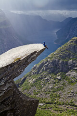 Man sitting on Trolltunga rock (Troll's Tongue rock) and makes the photo with the Norwegian mountain landscape