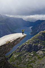 Girl standing on Trolltunga rock (Troll's Tongue rock) and makes the photo with the Norwegian mountain landscape