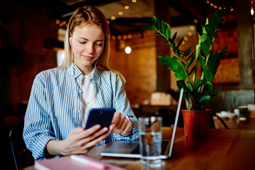 Young woman sitting at table and using smartphone in cafe