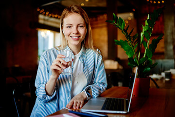 Smiling woman sitting at table with glass of water in hand in cafe