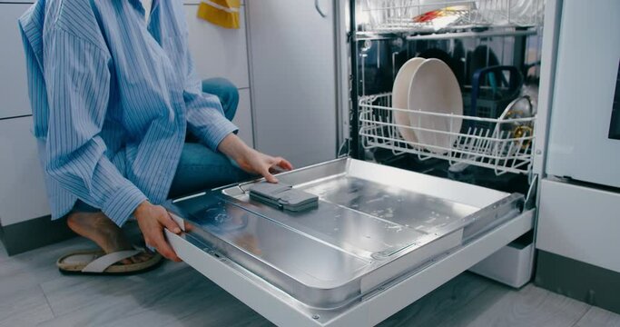 Woman putting detergent tablet into dishwasher machine, medium shot