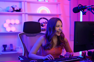 Close-up of Asian young adult woman sitting at gaming table and playing an online game with friends. A female gamer is overjoyed and feels happy after winning a multiplayer game with her teammate.