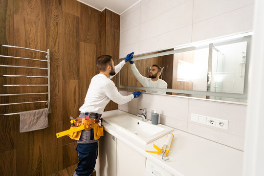 Man installing a mirror on wall in his renewed bathroom