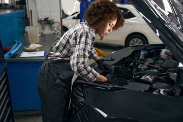 Young woman checks the engine under hood of a car