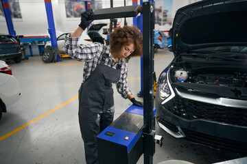 Young repairwoman uses special equipment for service maintenance of car