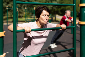 Obraz premium Aged woman doing exercises on sports bars in open-air sports area