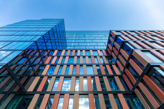 Wroclaw, Poland - June 2022: Upward view of a tall and modern office building full of glass windows reflecting the walls, decorations and blue blue sky