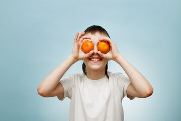 happy smiling boy with two mandarins covering his eyes on blue background.